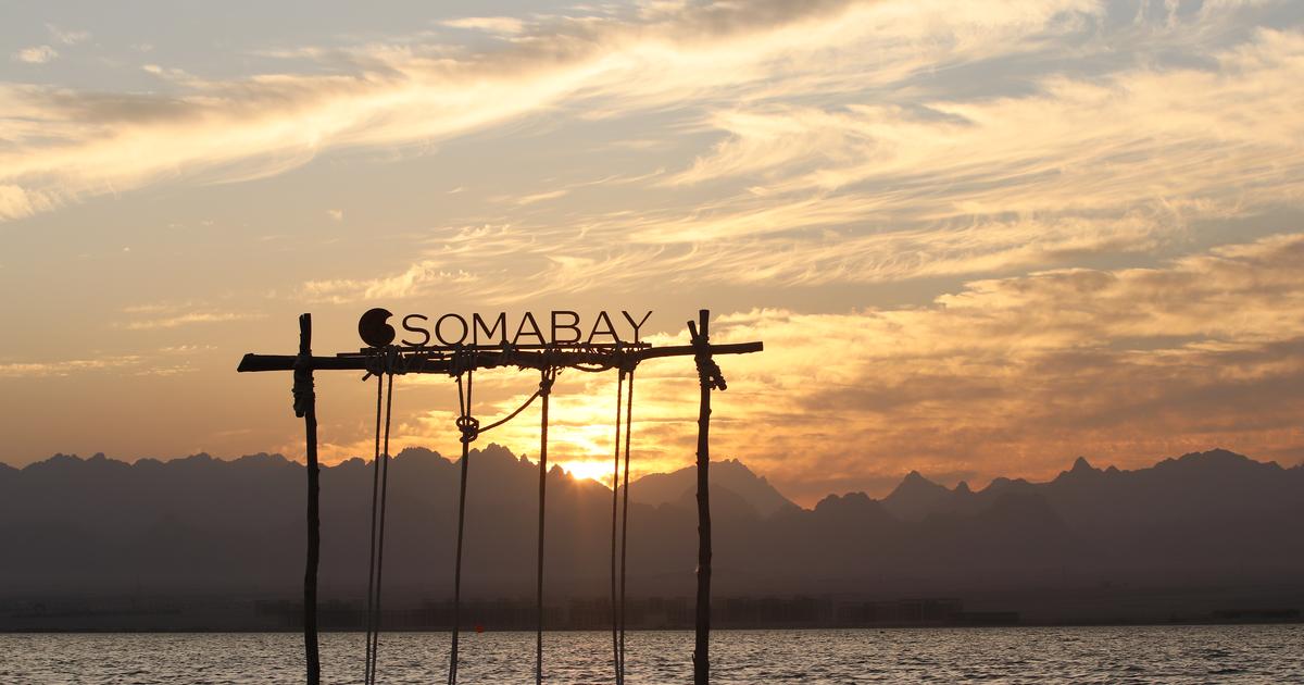 Somabay sign silhouetted against a dramatic sunset over the Red Sea, with mountains in the background