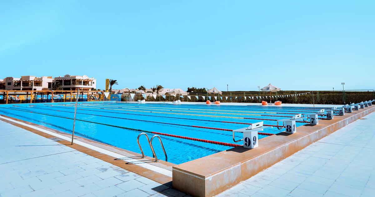 Empty Olympic-size outdoor swimming pool with numbered starting blocks and lane ropes under a clear blue sky