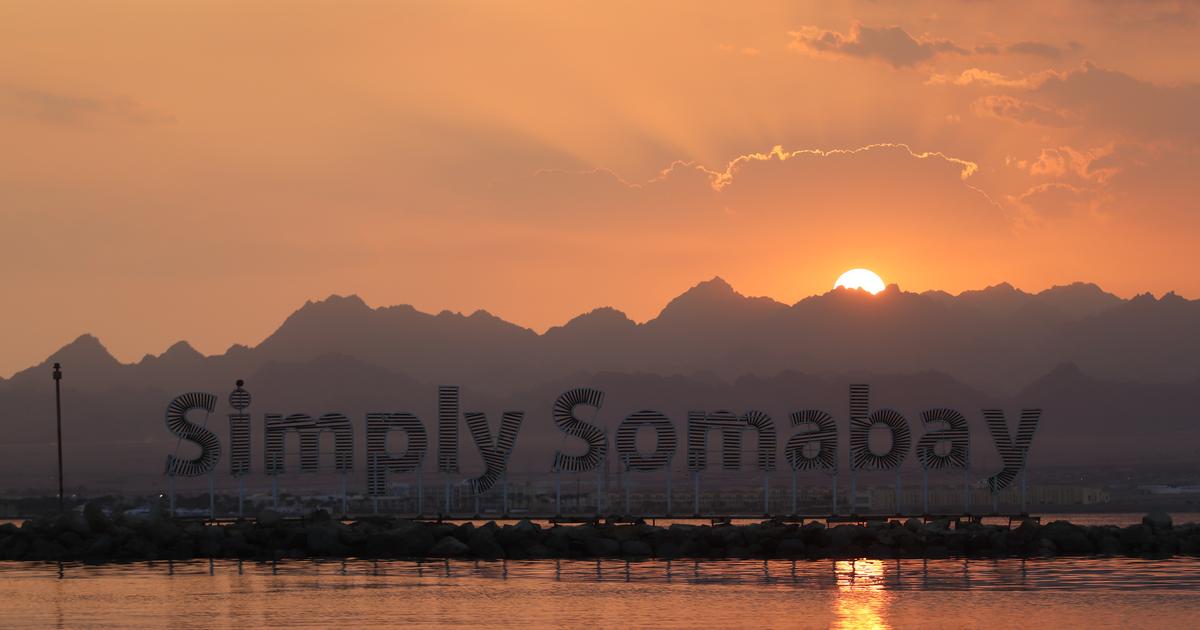 Знаковая вывеска Simply Somabay в силуэте на фоне пылающего заката над Красным морем с драматичным горным фоном и спокойными отражениями на воде